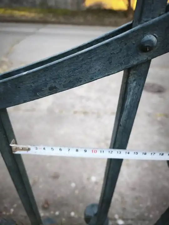 Pergő, oxidálódott festésű kovácsoltvas felület közelről, mérőszalaggal